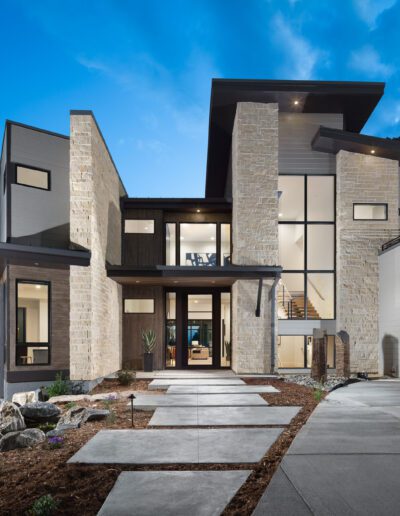 Modern two-story house with stone facade and large windows at dusk.