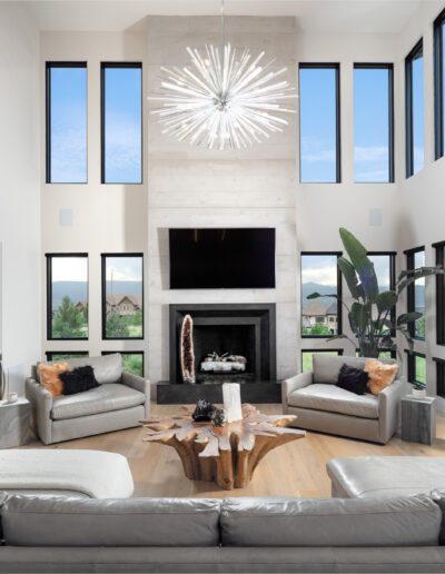 A spacious modern living room with high ceilings, large windows, a fireplace, and stylish furniture.